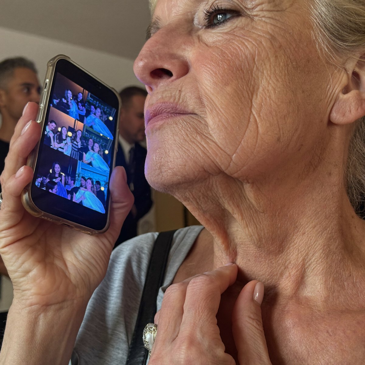 Mujer mirando las fotos de la celebración en el móvil mientras se toca la piel del cuello
