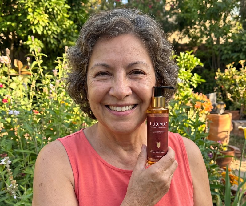 Mujer de unos 63 años con el aceite LUXMA junto a la cara, en su jardín